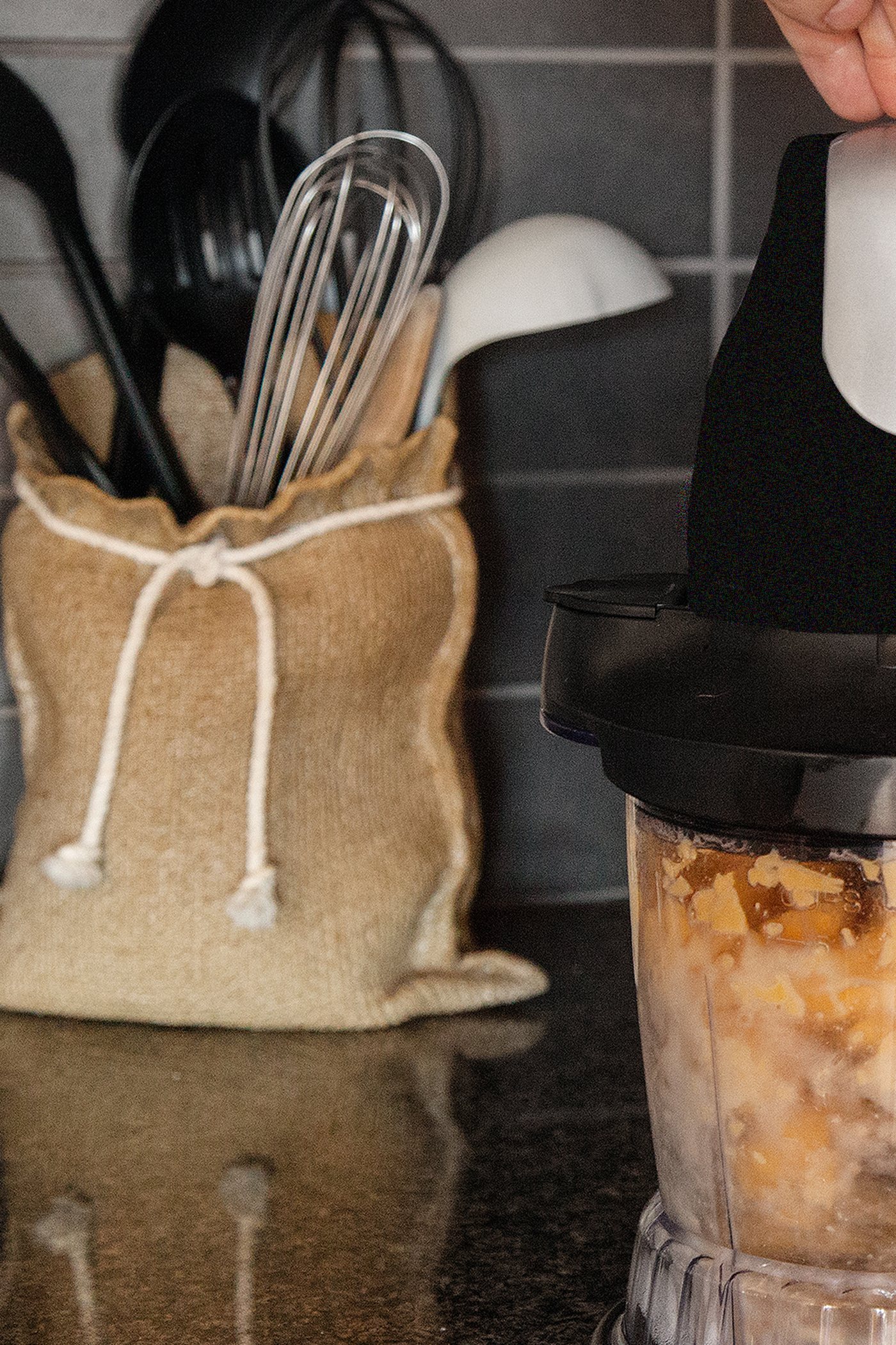Kitchen utensils in a white crock beside fresh herbs