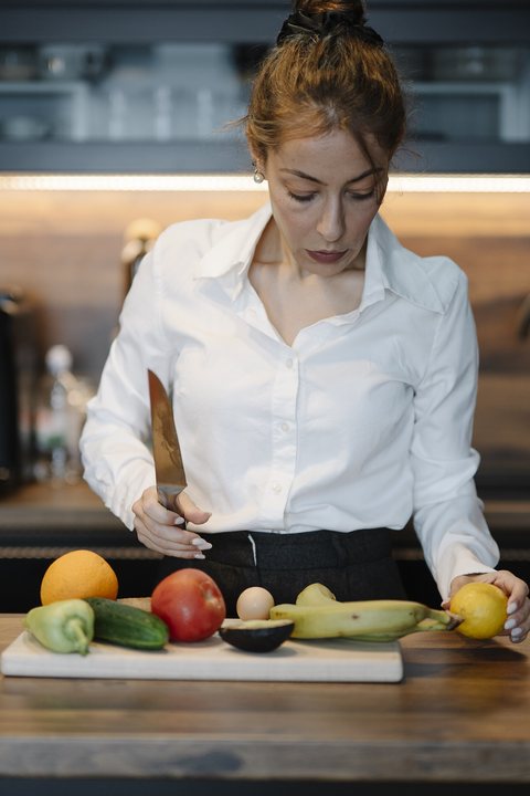 Maya Ellison adding fresh herbs to a pot in her kitchen